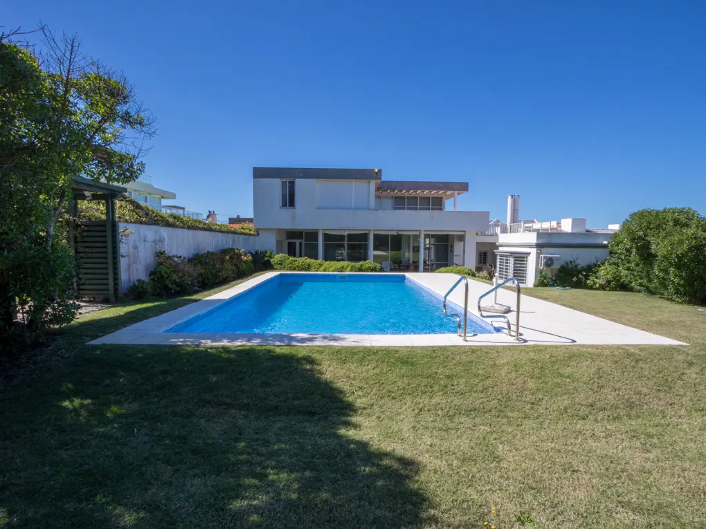 Modern white house with a rectangular blue swimming pool in a grassy backyard under a clear blue sky.