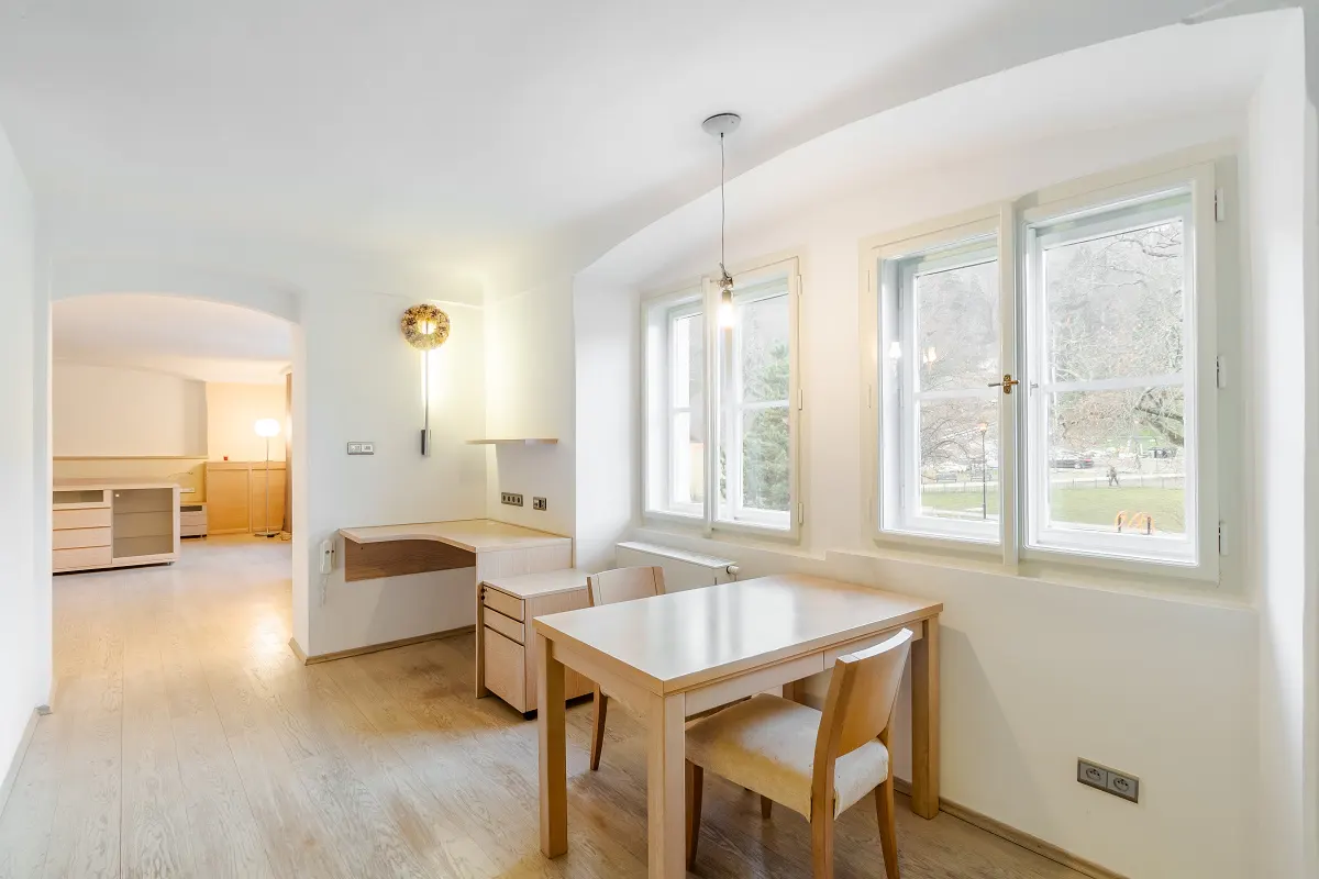 Bright, airy room with light wood floors, a table and chairs, and a built-in desk. Large windows overlook a park.