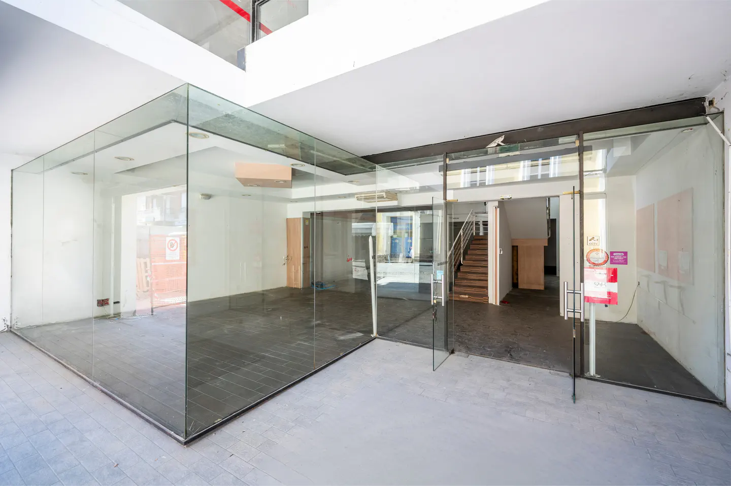 Empty commercial space with glass walls and doors, white walls, and gray floors. Stairs are visible in the background.