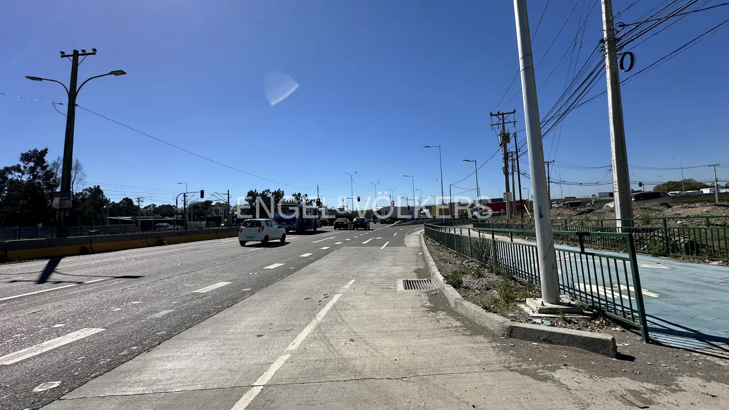 Street view with cars on a sunny day. A white car is driving on the left lane. A blue sky is above.