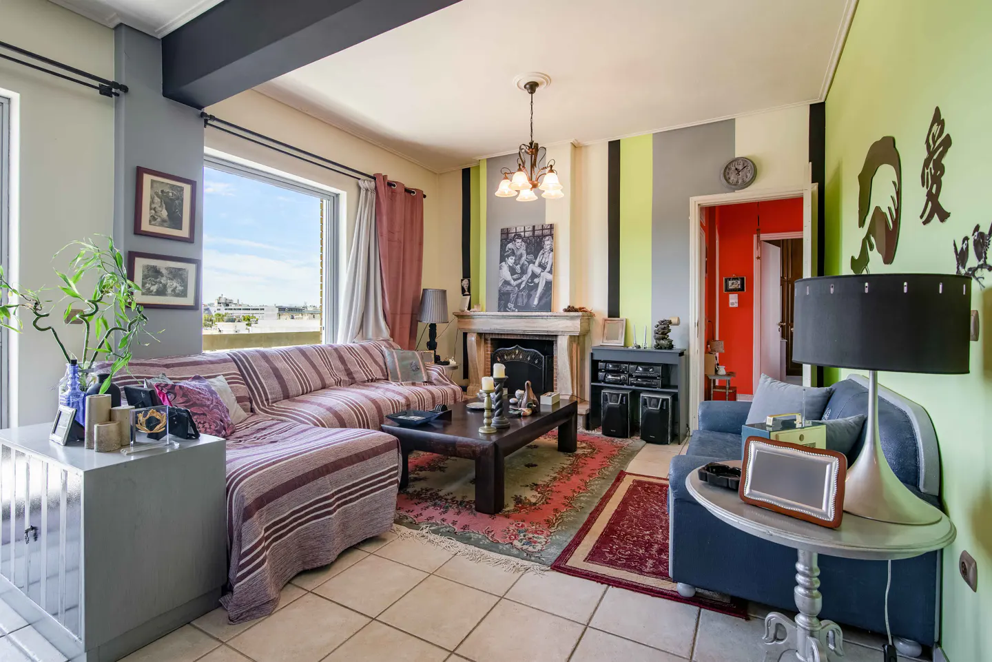 Living room with striped walls, a fireplace, and a large window. A striped sofa and a blue loveseat provide seating.