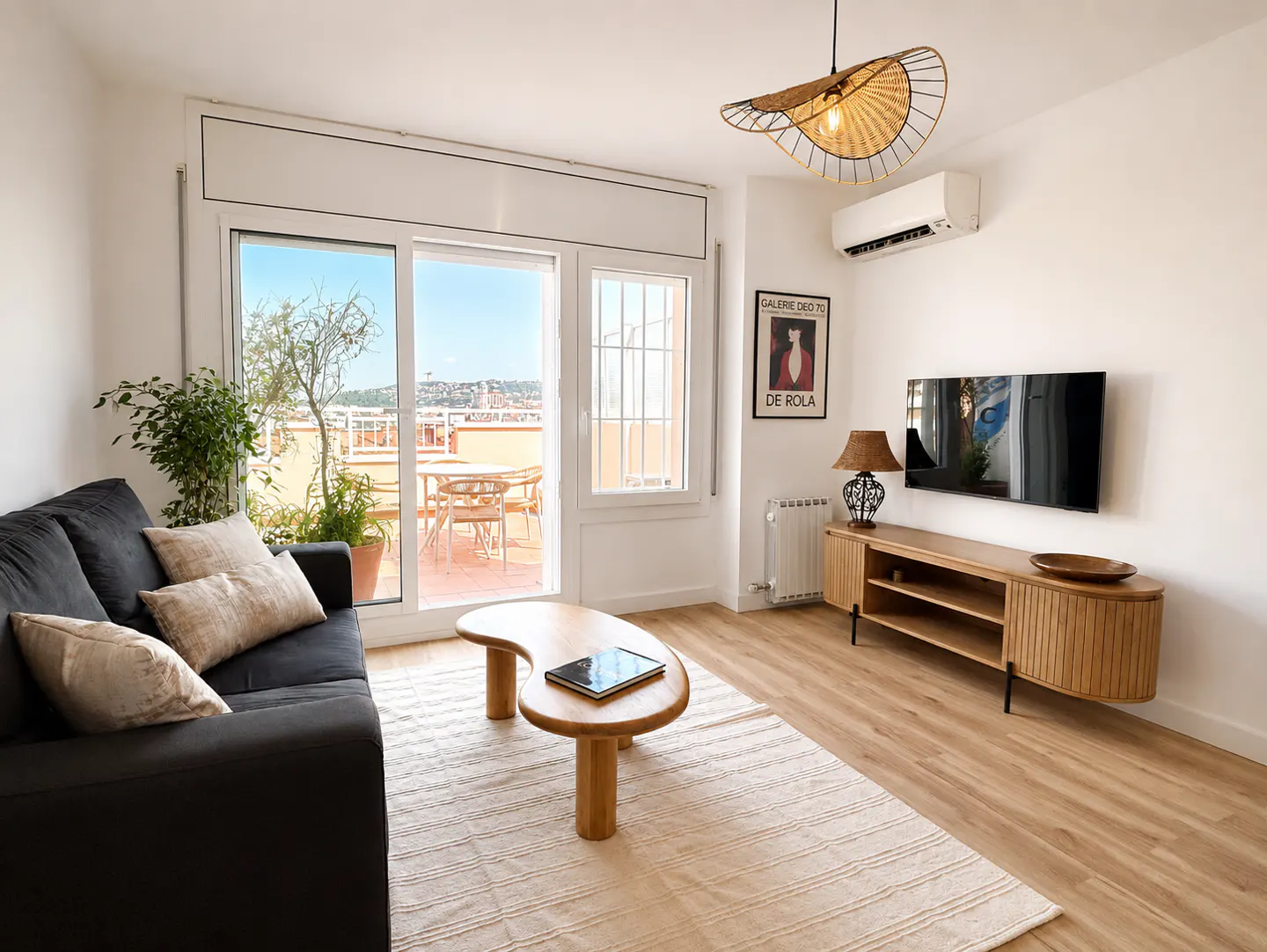 Bright living room with a black sofa, wooden coffee table, TV, and a balcony with a view.