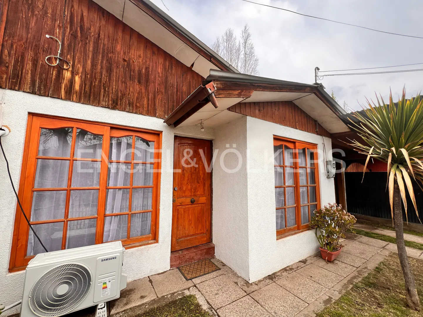 Exterior of a white house with wood trim, orange door and window frames, and Engel & Völkers logo.