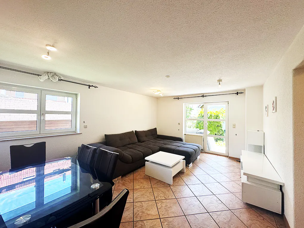 A bright living room with a brown sectional sofa, a white coffee table, and a black dining table with chairs.