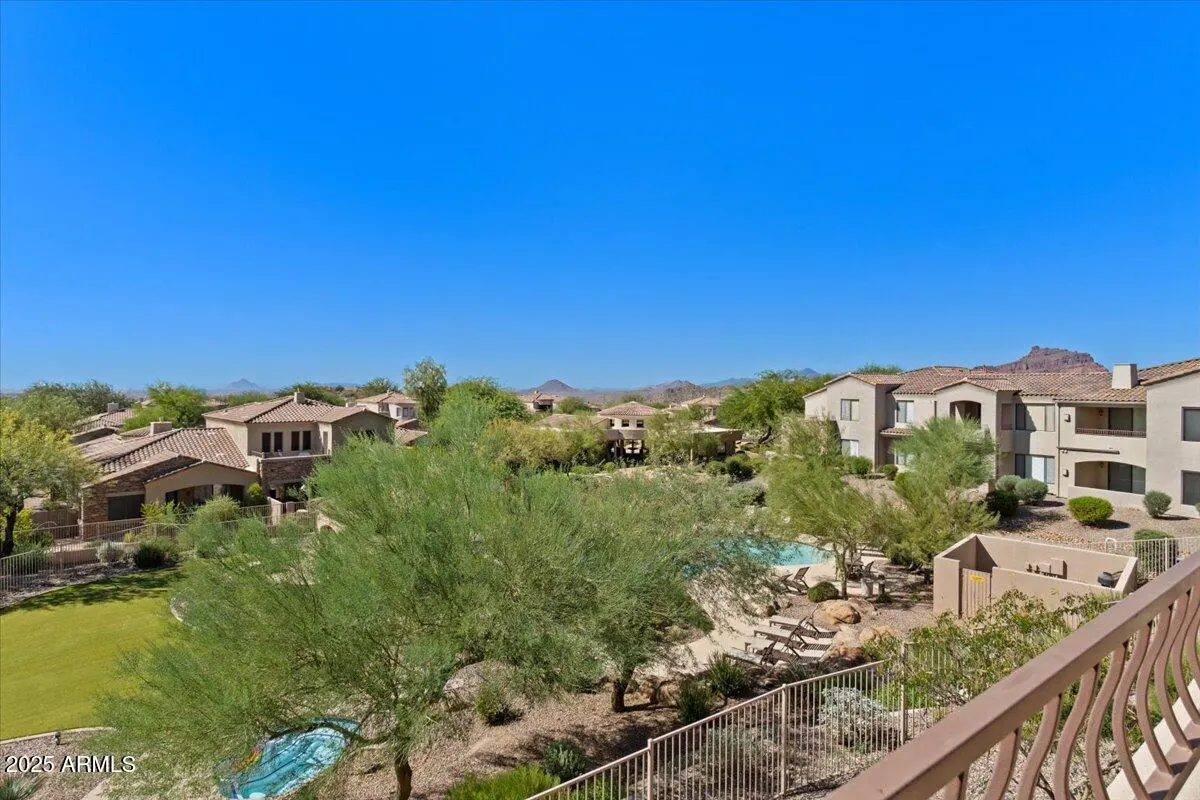 Scenic view of desert homes with terracotta roofs, lush green trees, and a community pool under a clear blue sky.