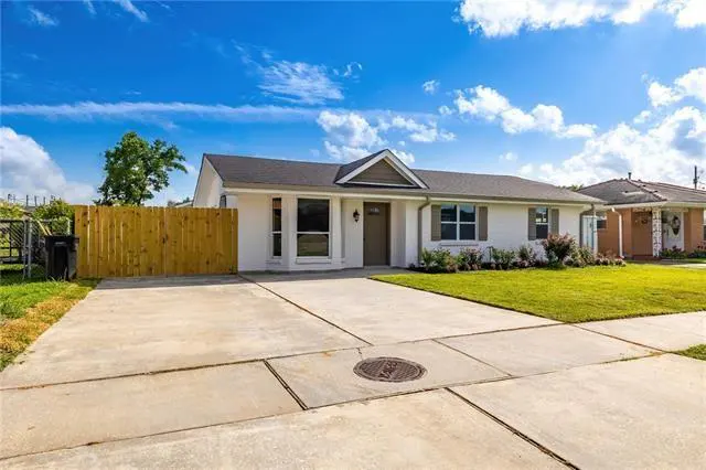 A white single-story house with a gray roof, brown door, and a concrete driveway under a blue sky.