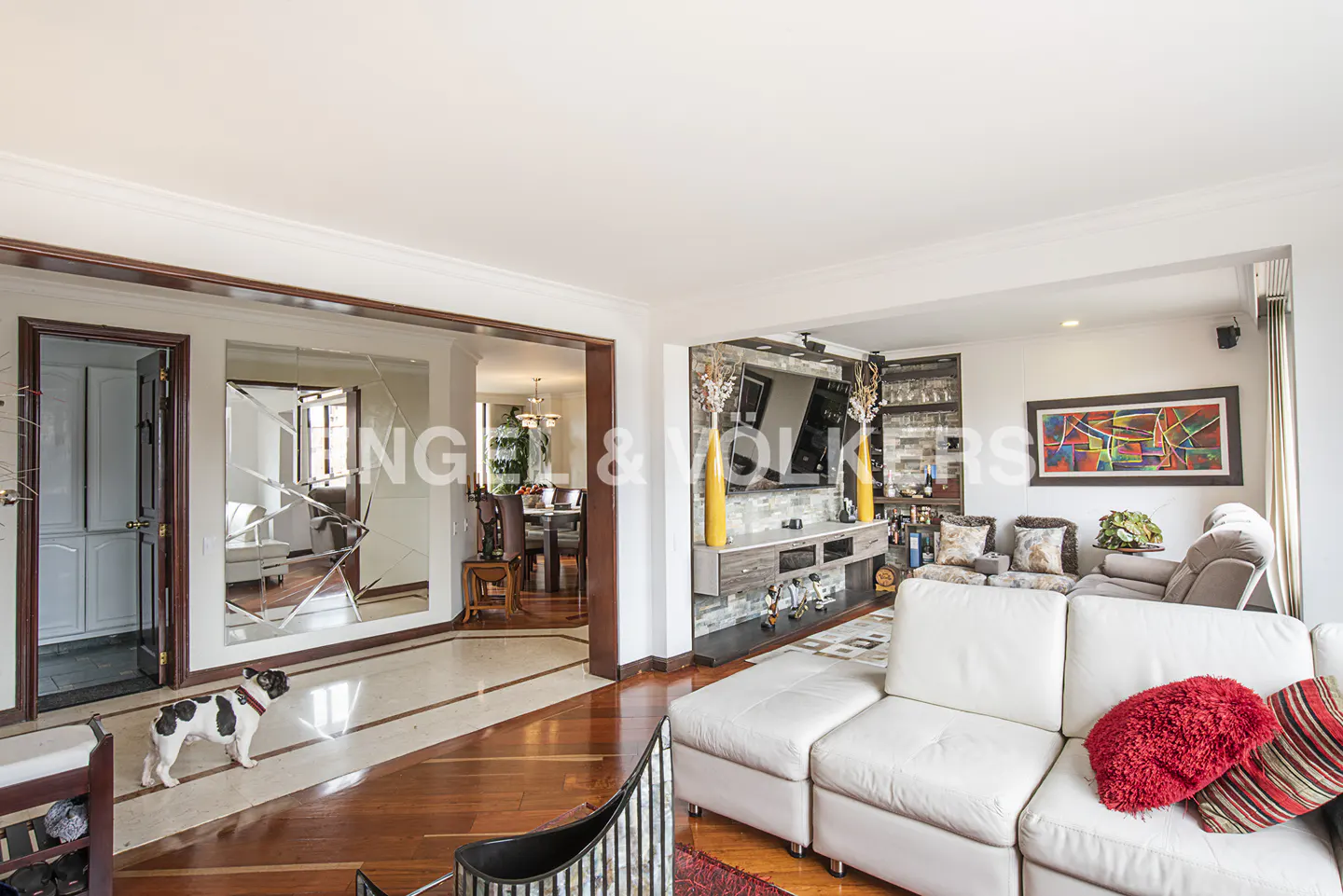 Bright living room with white sectional sofa, hardwood floors, a French bulldog, and a stone-accented media wall.