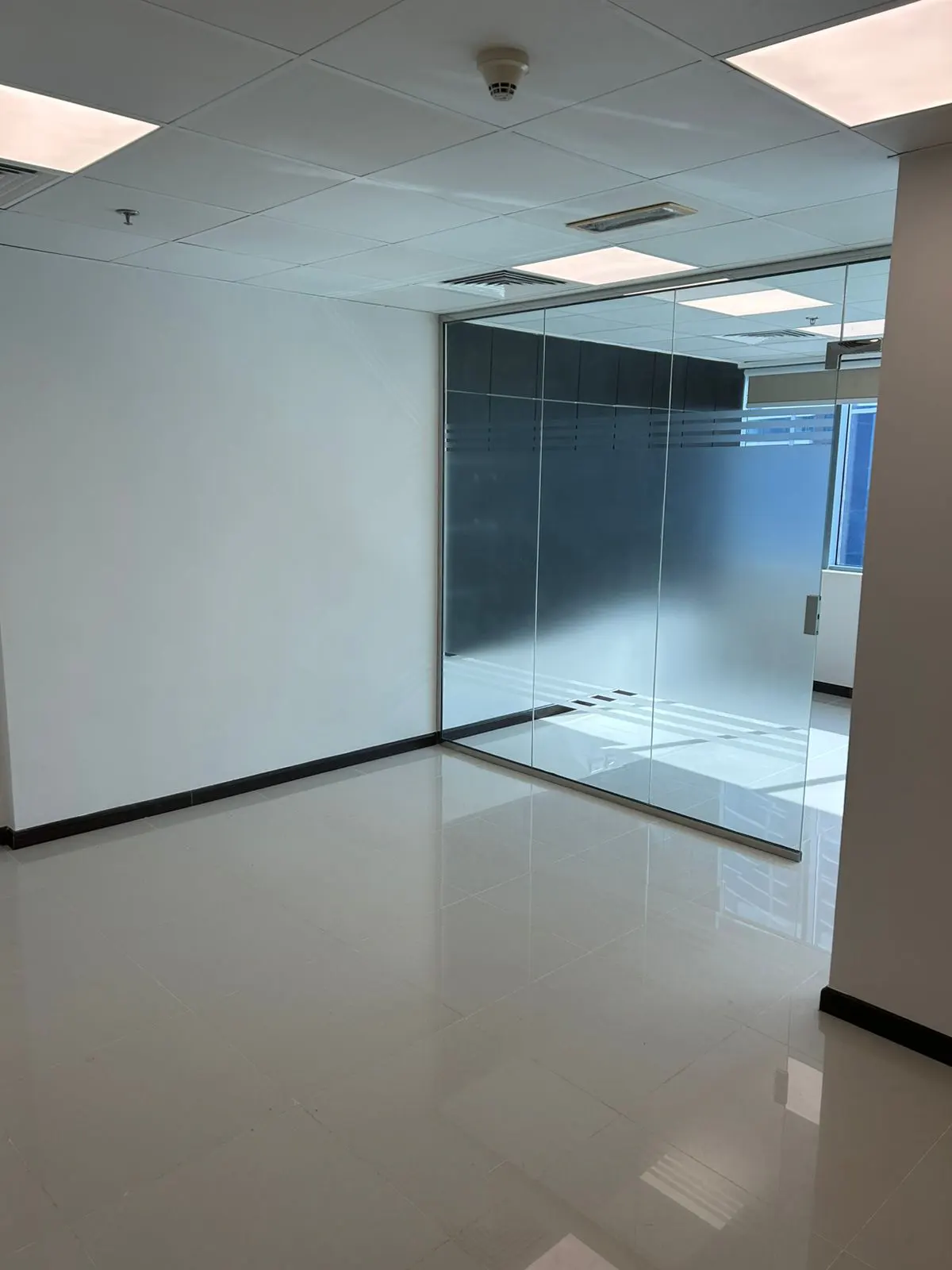 Empty office space with white walls, glossy tile floor, and glass-walled room with frosted privacy film.