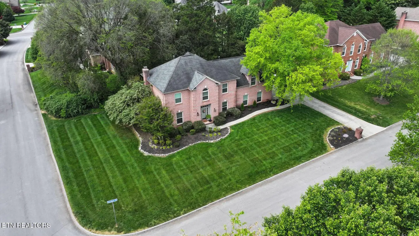 Aerial view of a two-story pink brick house with a gray roof, surrounded by a green lawn and trees.