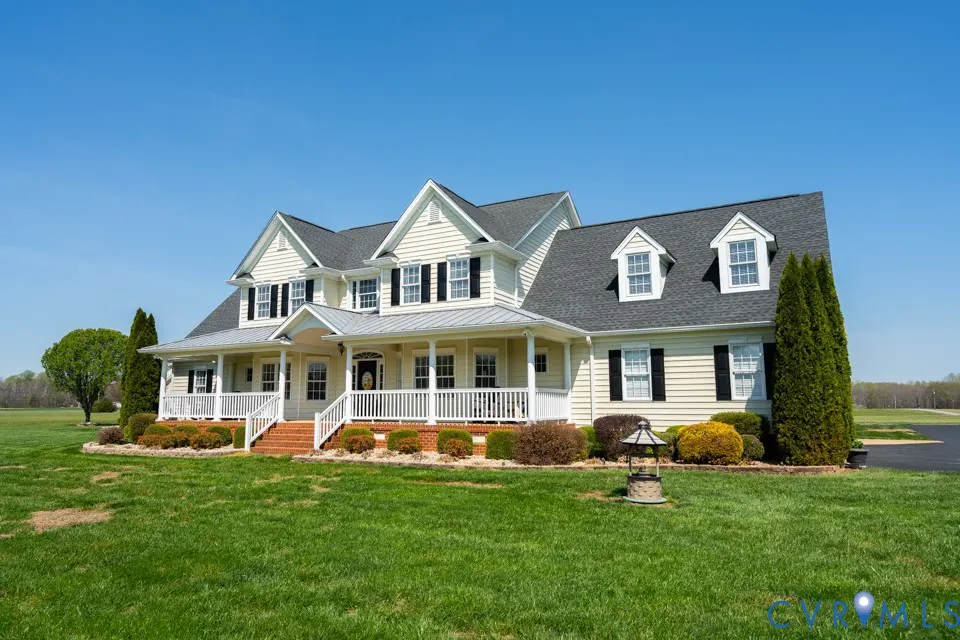 Beige two-story house with black shutters, gray roof, and white porch under a clear blue sky.