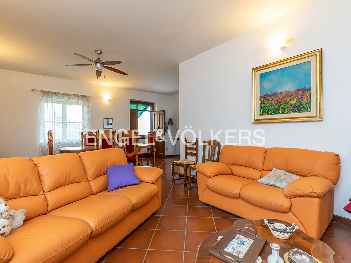 Living room with orange sofas, terracotta tile floor, and a painting on the wall. A ceiling fan is visible.