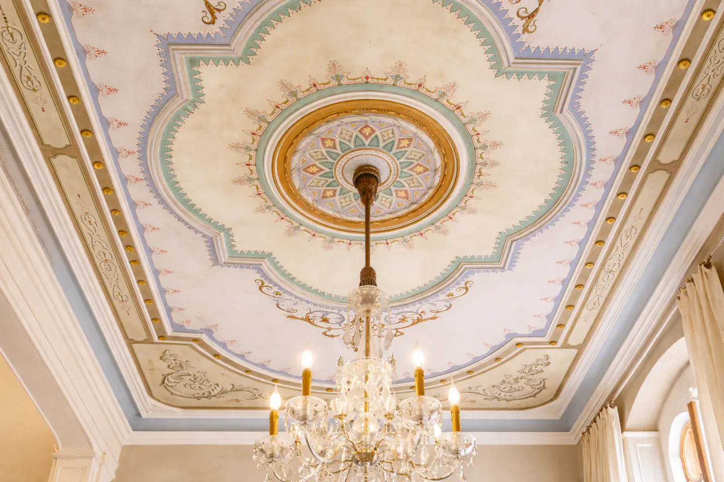 Ornate ceiling with painted floral designs in pastel colors, and a crystal chandelier with lit candles hanging from the center.