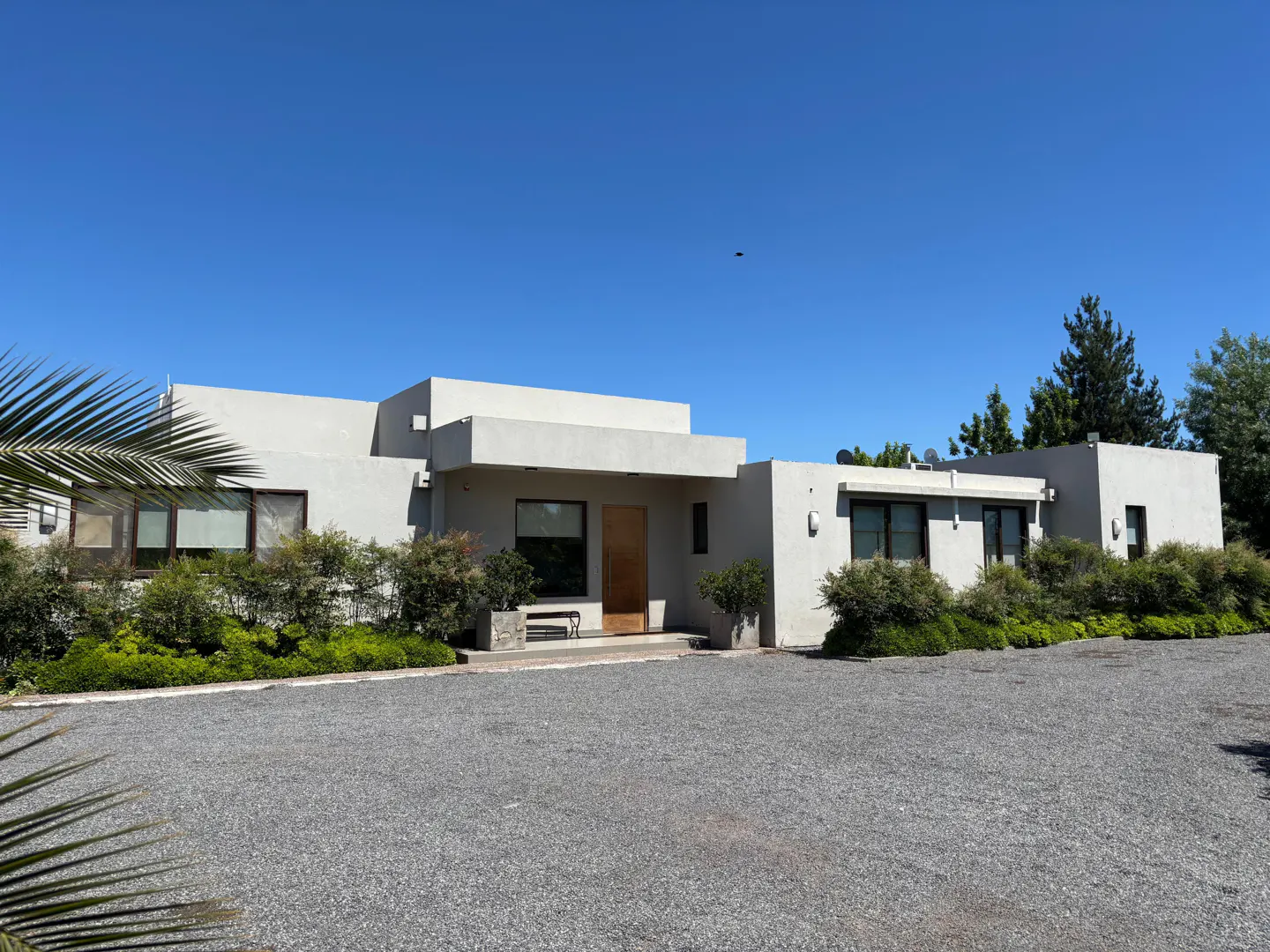 Modern, single-story home with a flat roof, gray exterior, and gravel driveway under a clear blue sky.