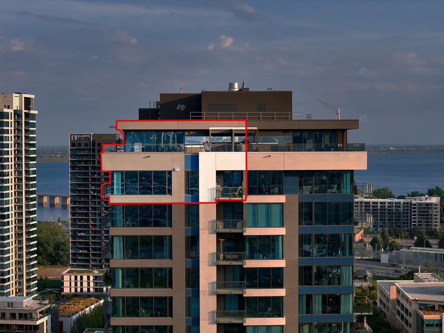Close-up of a modern high-rise building with blue glass windows and a beige facade. A balcony with two people is visible.