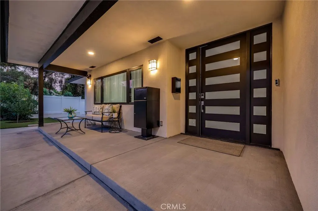 Covered porch with a modern front door. A black mailbox stands near the door. A small seating area is visible on the left.