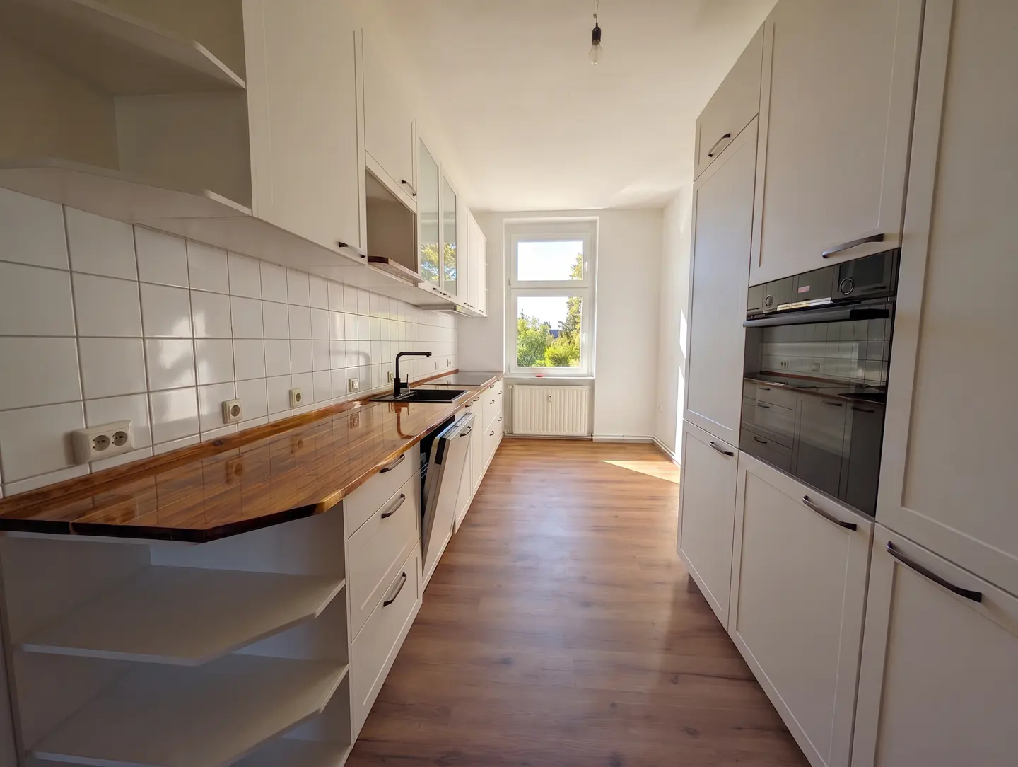 Bright kitchen with white cabinets, wood countertop, and wood floor. A window lets in natural light.
