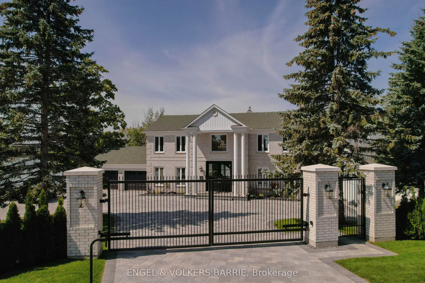 Exterior view of a large, two-story white brick house with black iron gates and tall green trees.