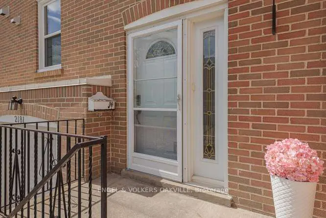 Brick house exterior with a white front door with decorative glass, a white mailbox, and a pink flower arrangement.