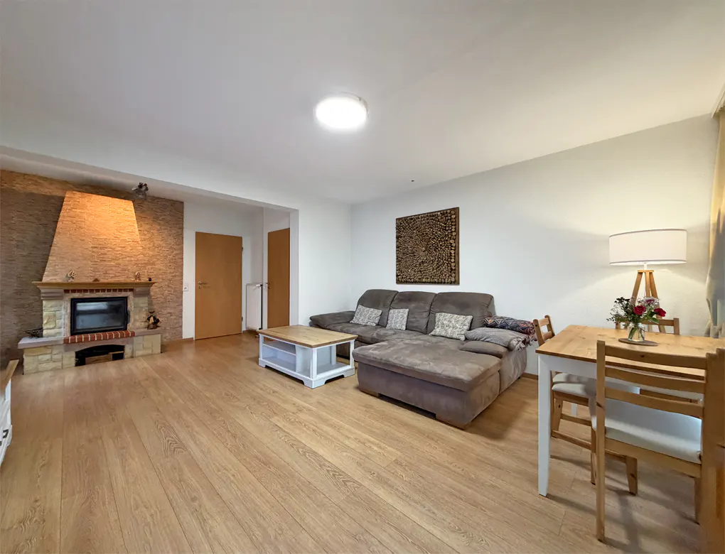 A living room with a fireplace, a brown sofa, a wooden table and chairs, and a wooden floor.