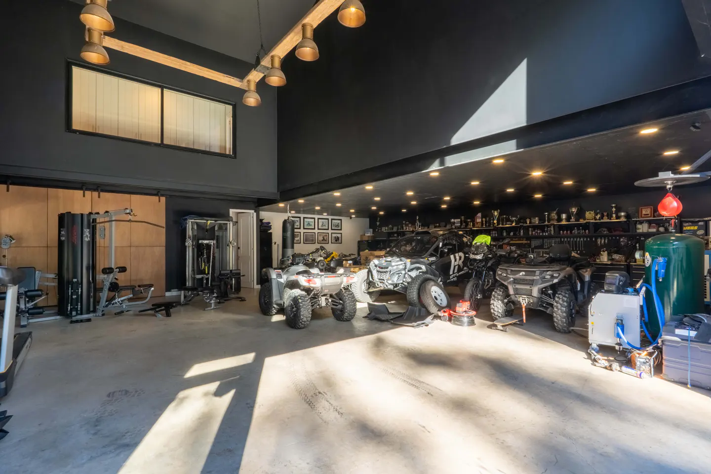A large garage with black ceilings, recessed lighting, ATVs, a motorcycle, and gym equipment.
