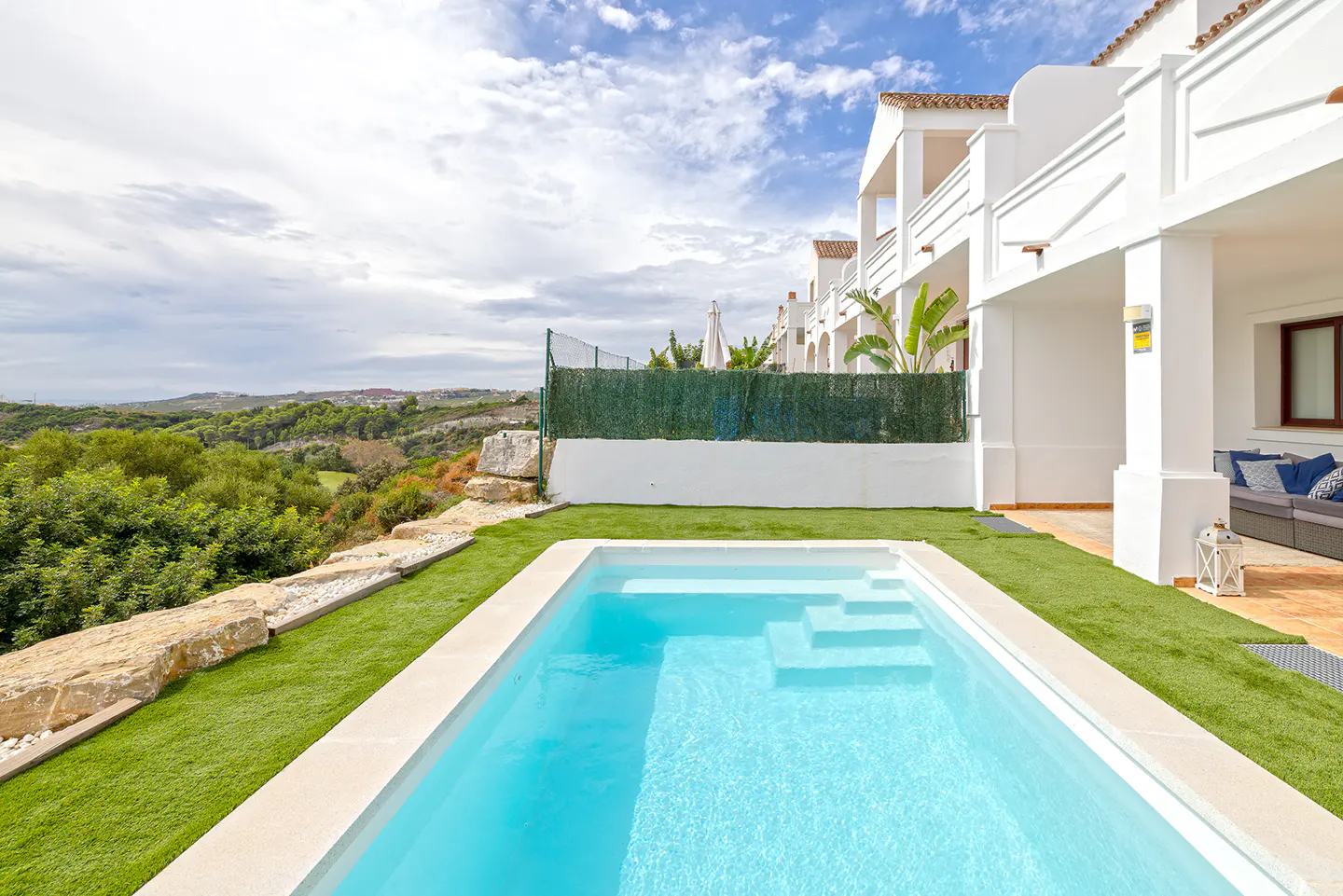Private swimming pool with turquoise water, green lawn, and white villa terrace overlooking a scenic hilly landscape.