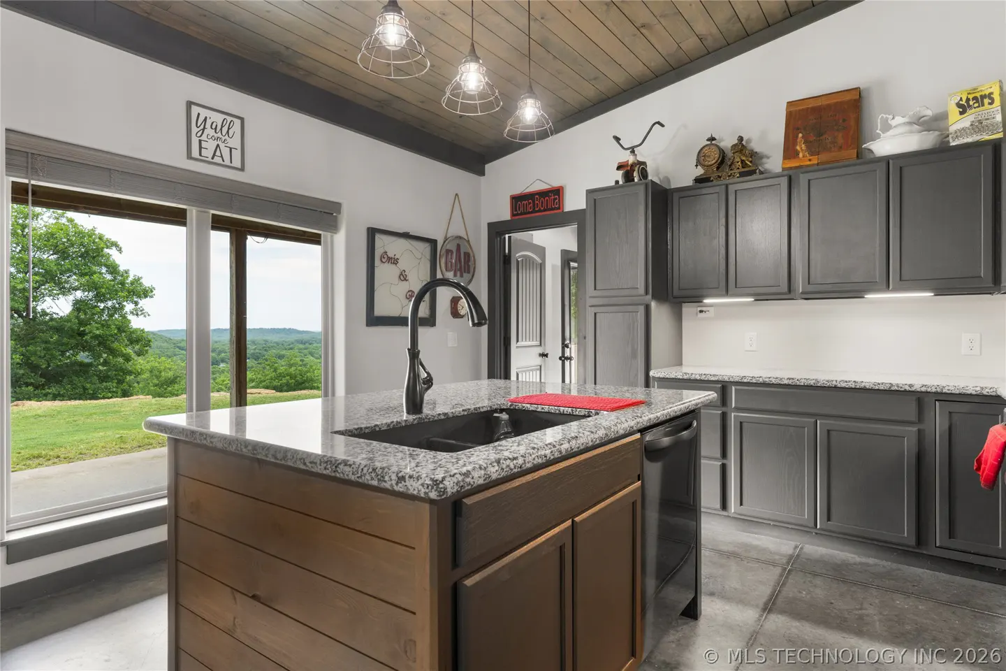 A modern kitchen with gray cabinets, a wood island with a granite countertop, and a large window with a view of green hills.