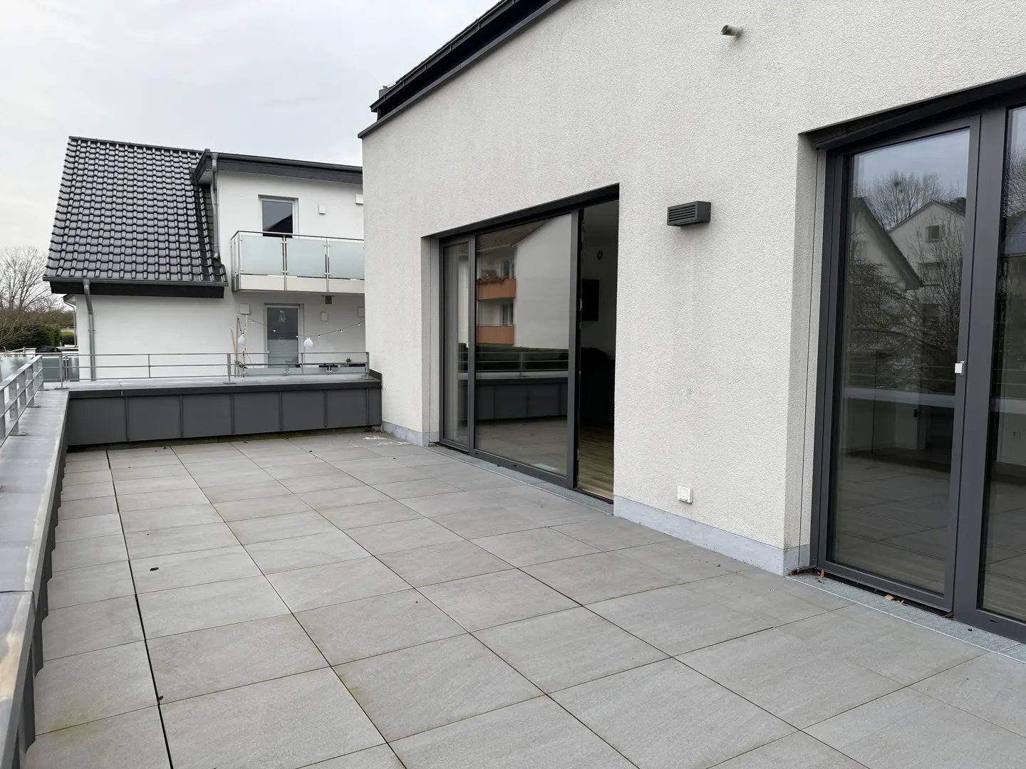 A gray tiled patio with sliding glass doors on a white building. Another building is visible in the background.