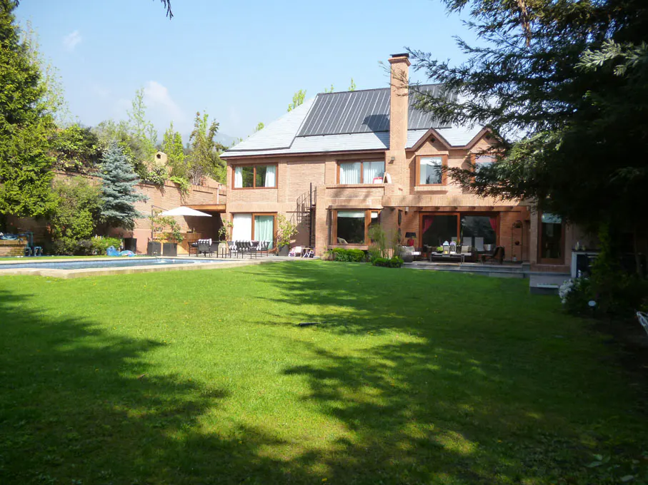 Brick house with a gray roof, chimney, and large windows. Green lawn, pool, and patio furniture in the backyard.