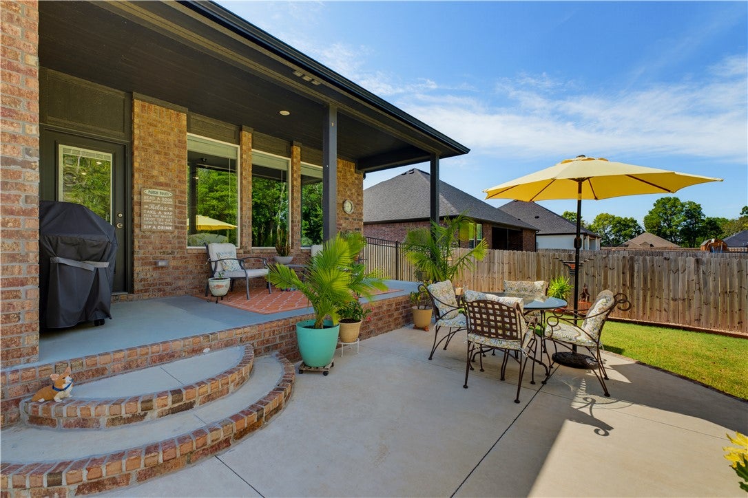 Back patio with brick steps, a covered area, outdoor dining set with yellow umbrella, and a fenced backyard. [AI-generated text]