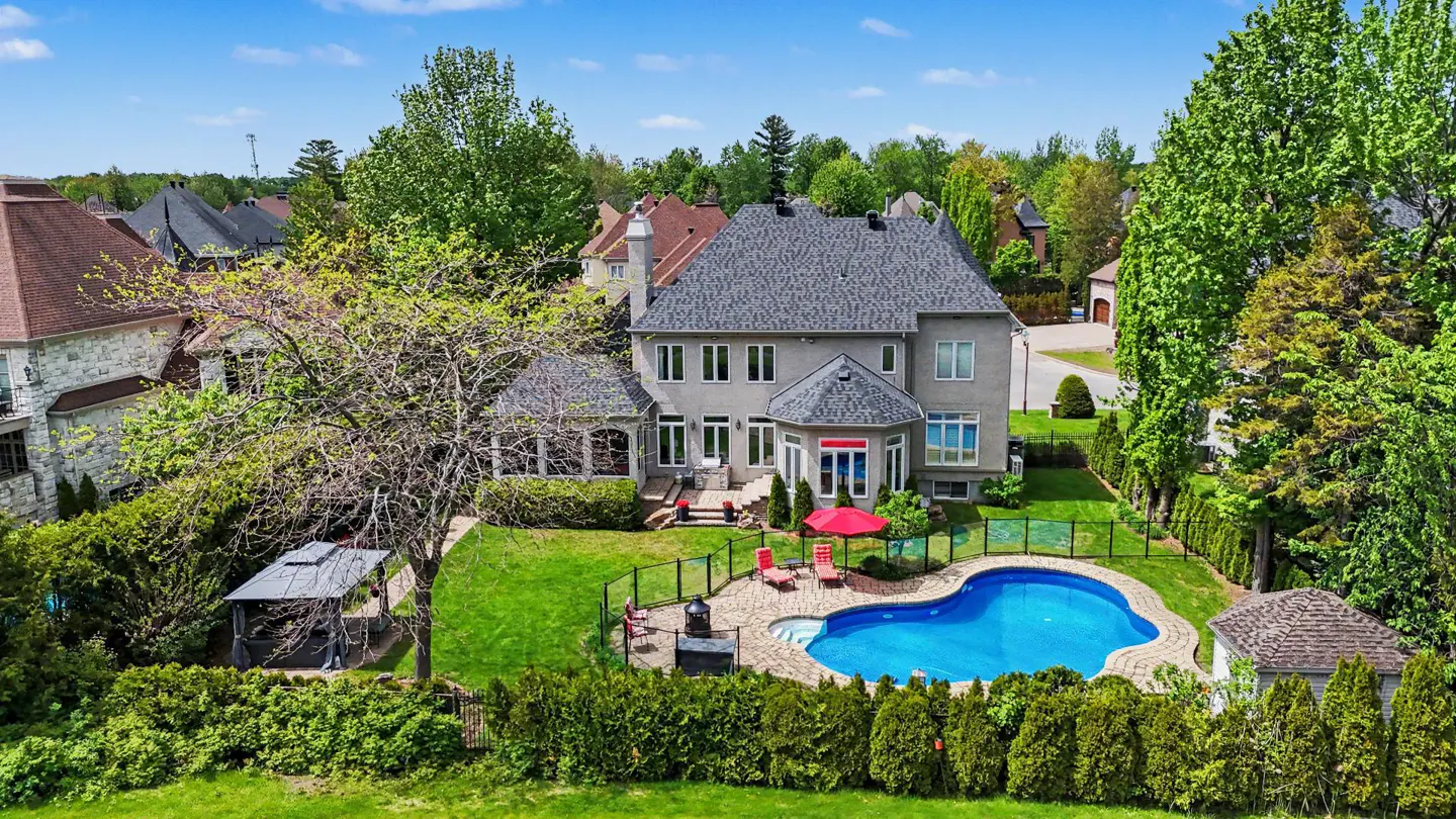 Aerial view of a gray two-story house with a pool, red umbrella, and green lawn.