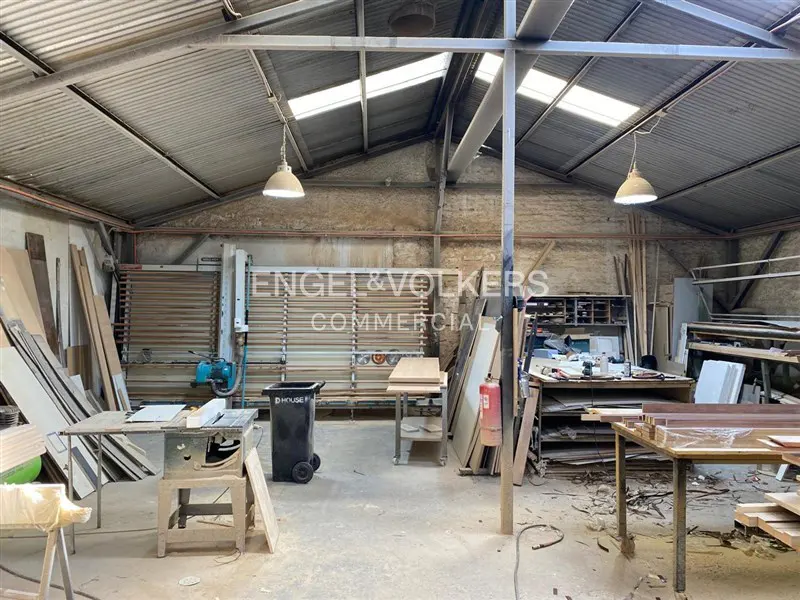 Interior view of a commercial woodworking shop with tools, lumber, and metal roof.