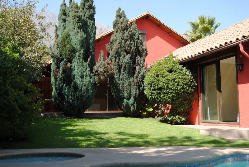 Red house with a tile roof, green lawn, trees, and a pool in the foreground.
