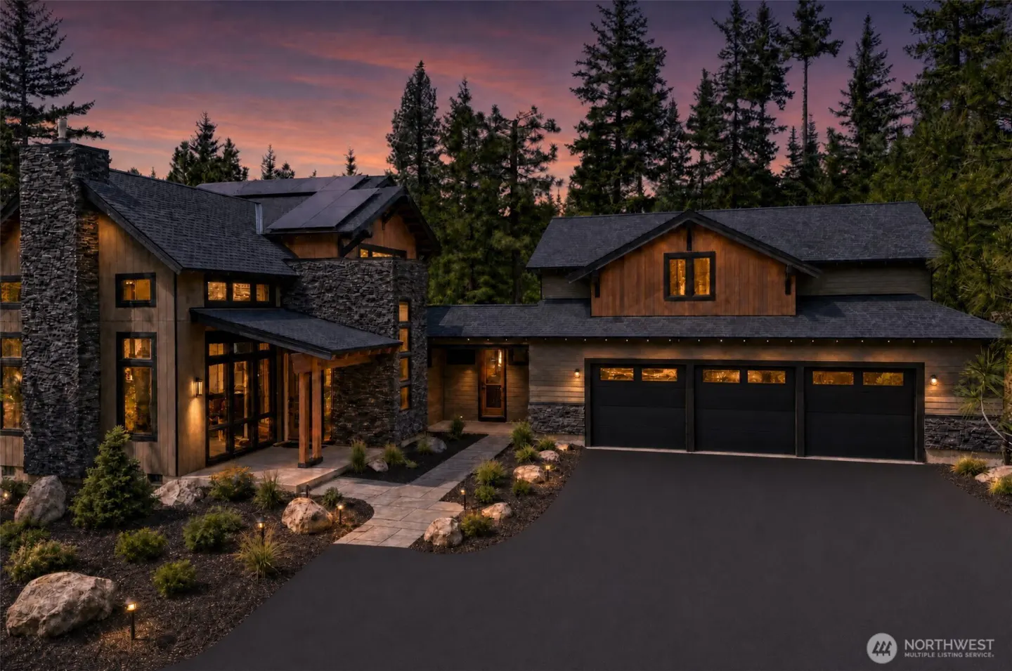 Exterior of a two-story home with stone and wood accents, a black roof, and a three-car garage at dusk.