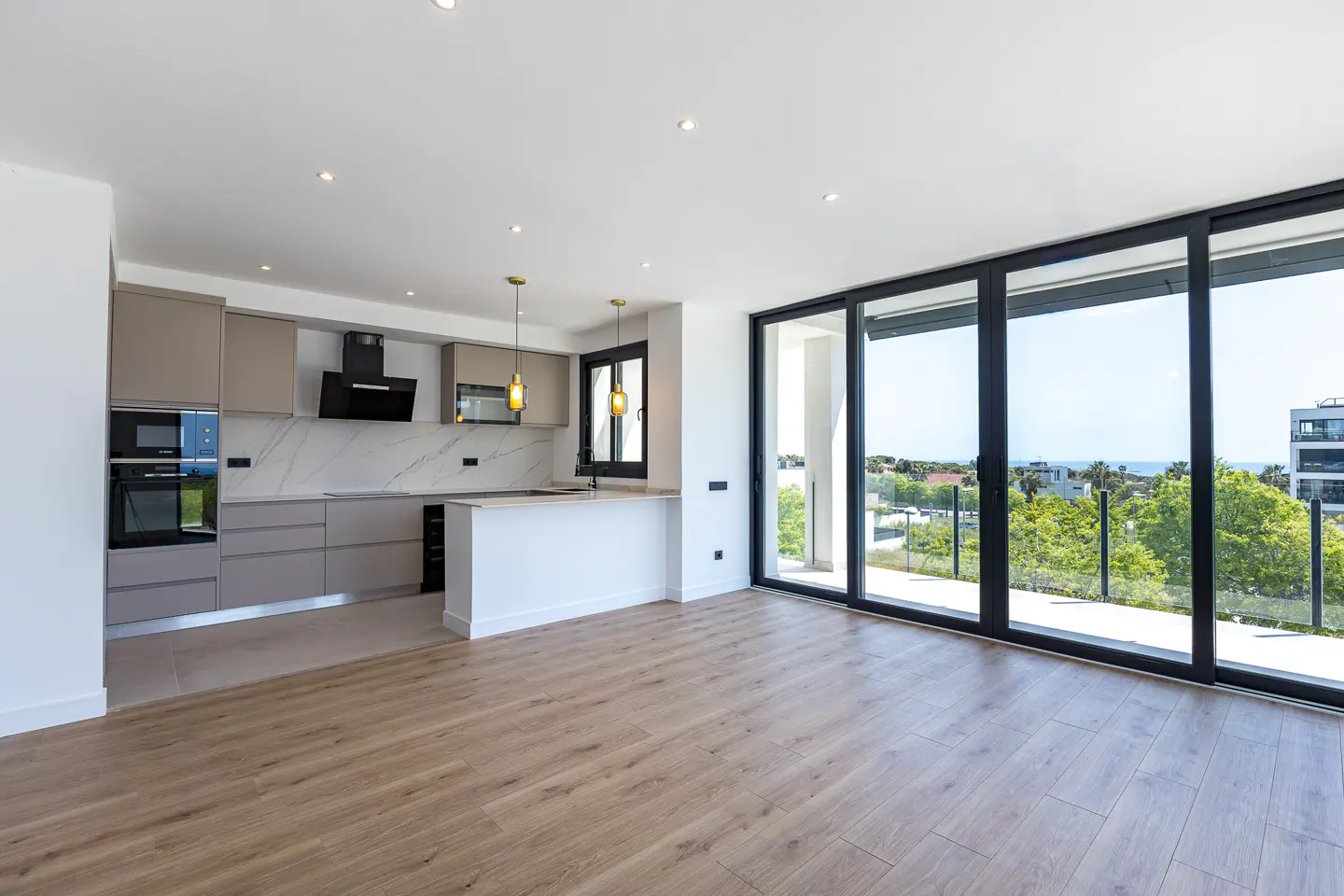 A modern, open-concept kitchen with gray cabinets, a white island, and large sliding glass doors to a balcony with a view.