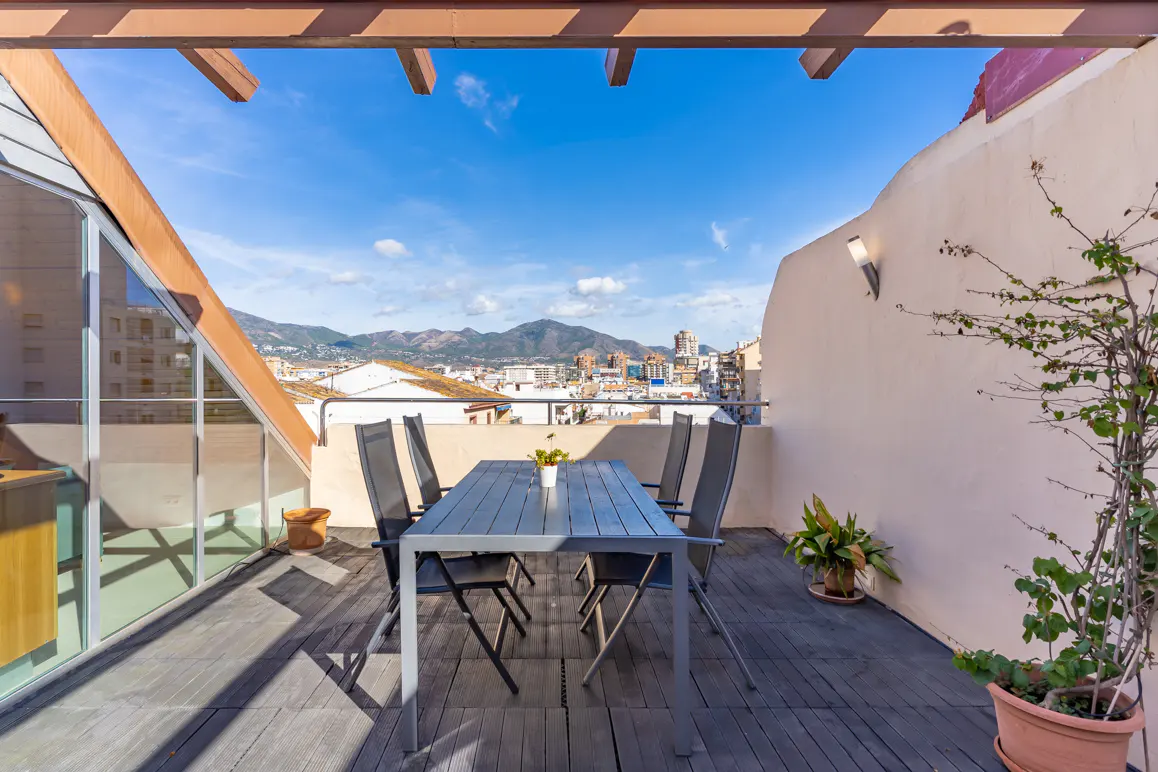 Rooftop terrace with a dining table, four chairs, potted plants, and a scenic view of the city and distant mountains.