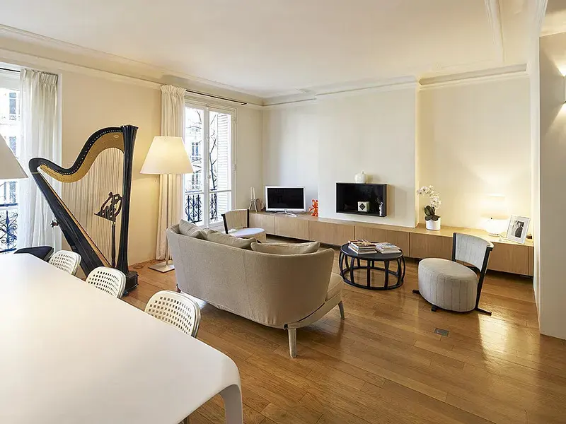 Bright living room with hardwood floors, a beige sofa, a harp, a round coffee table, and a wall-mounted television.