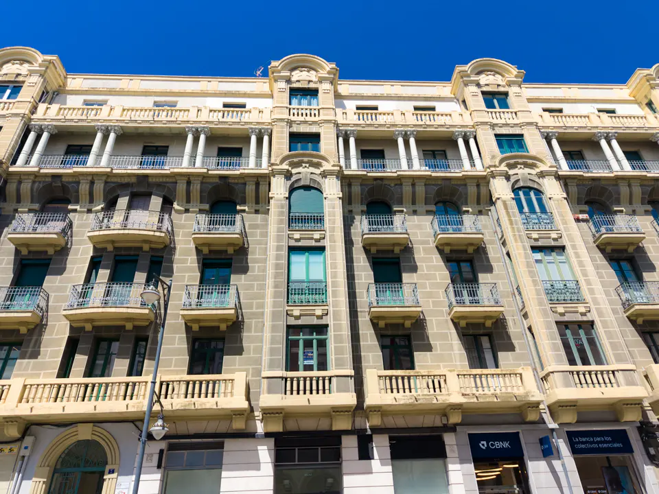 Exterior view of a multi-story building with balconies and columns under a clear blue sky.