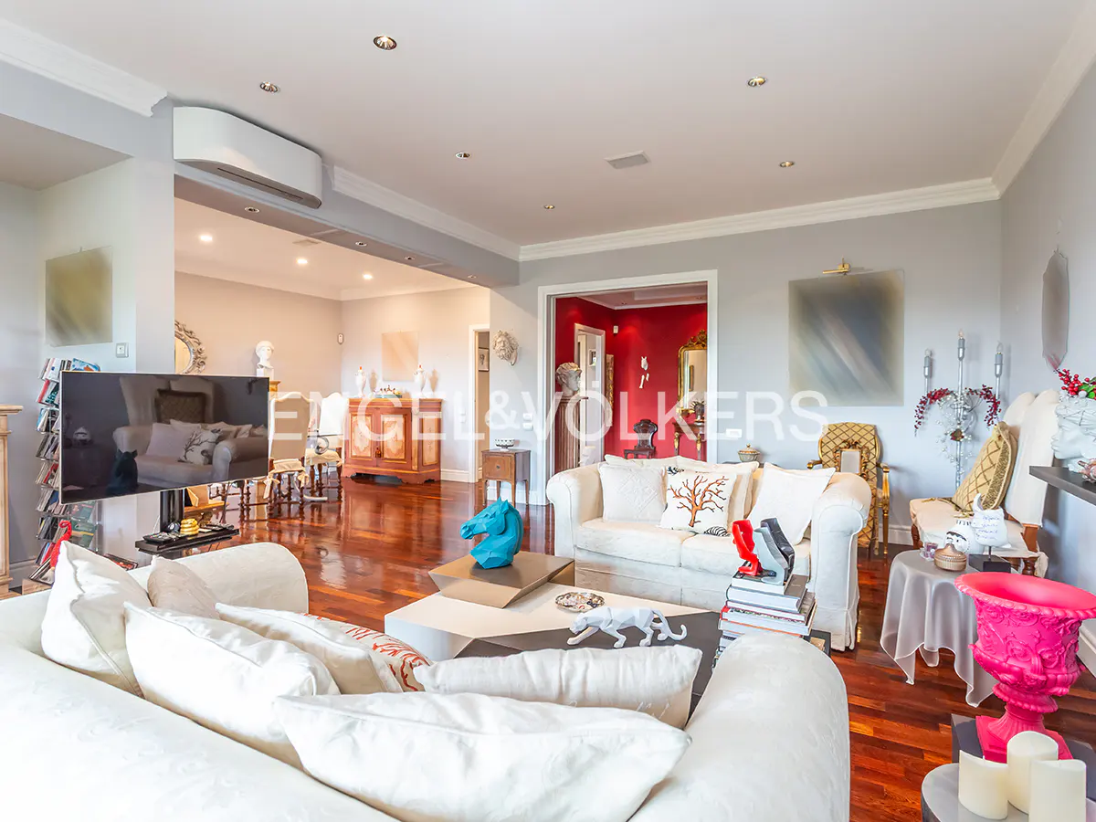Spacious living room with white sofas, hardwood floors, a bright pink decorative urn, and a view into a red-walled room.