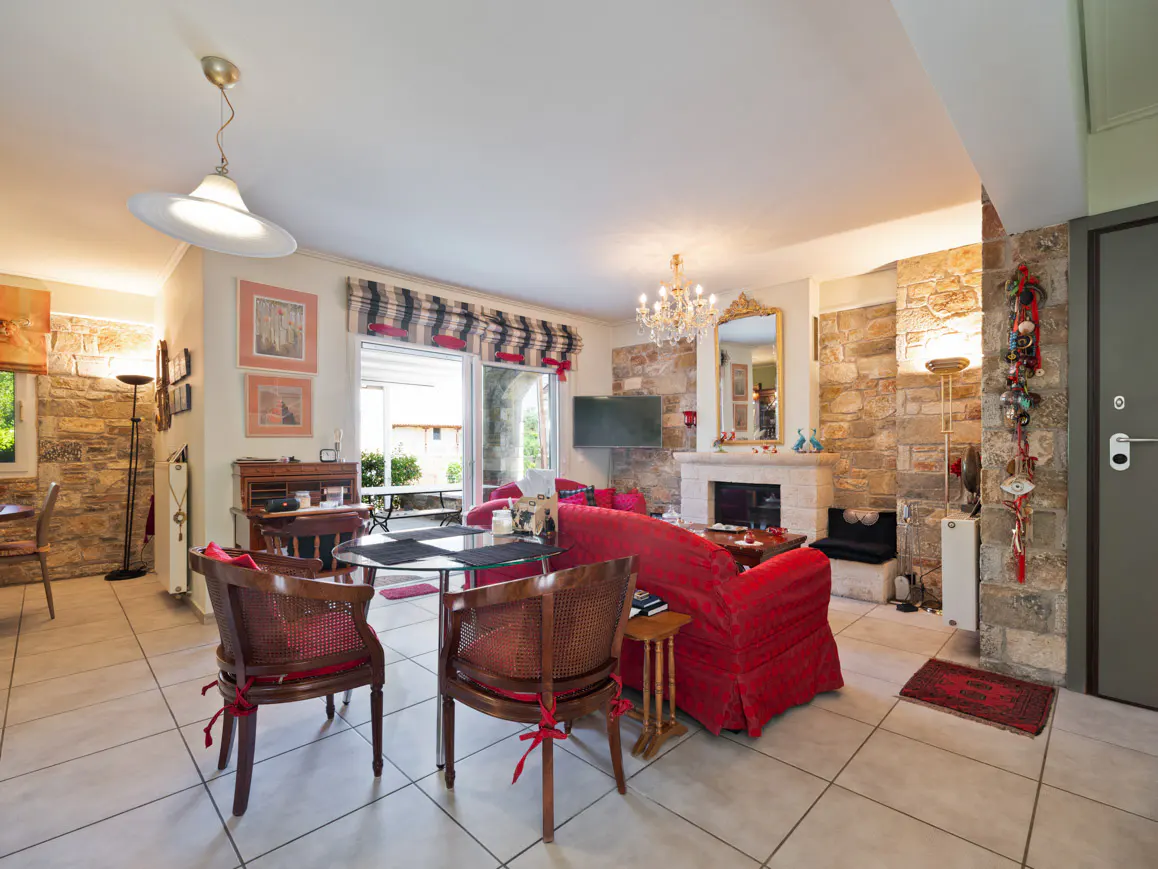 Living room with stone walls, a red sofa, a glass dining table with two wooden chairs, and a fireplace with a mirror.