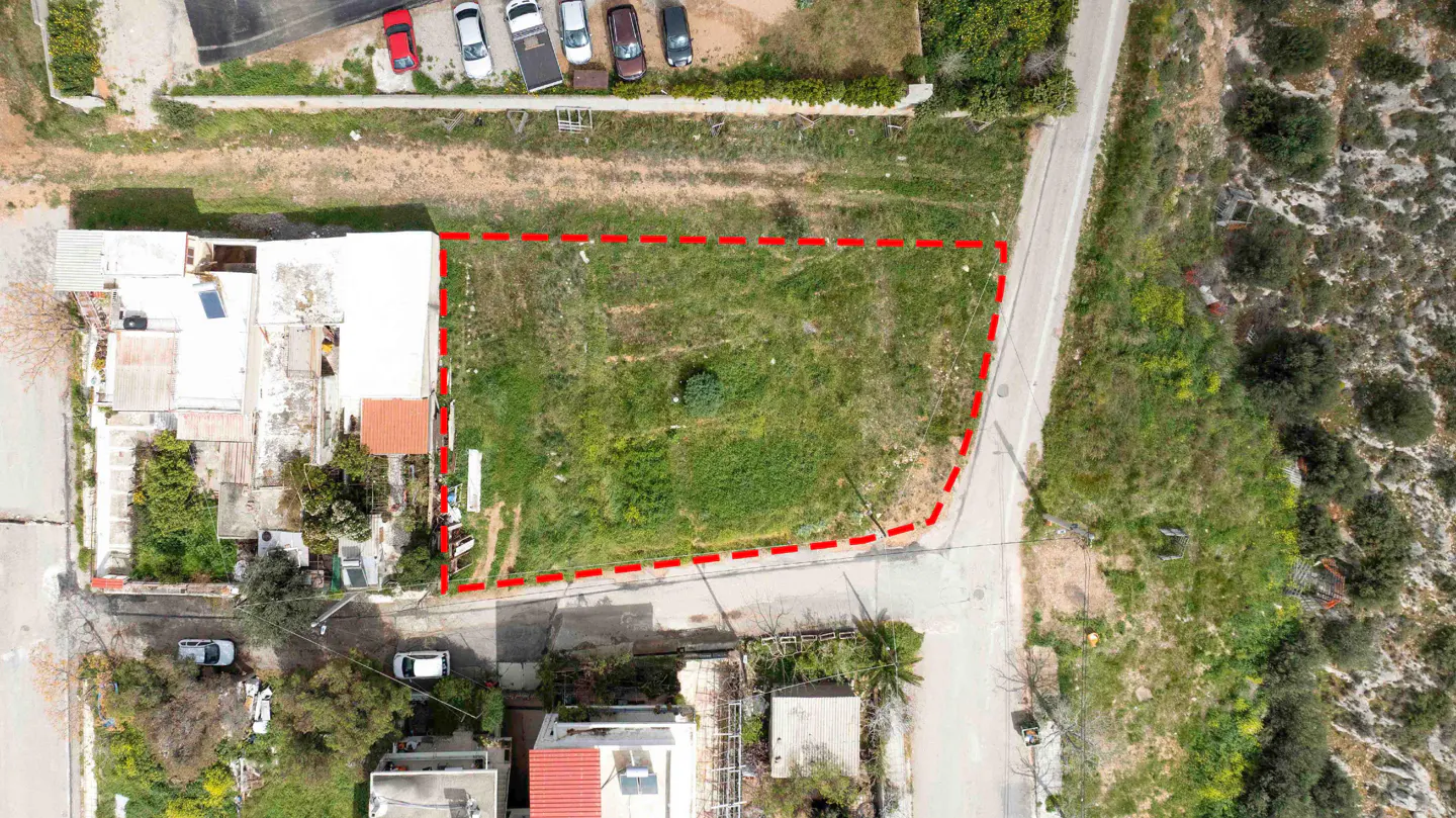 Aerial view of a vacant rectangular plot of land outlined in red, situated between residential buildings and a road.