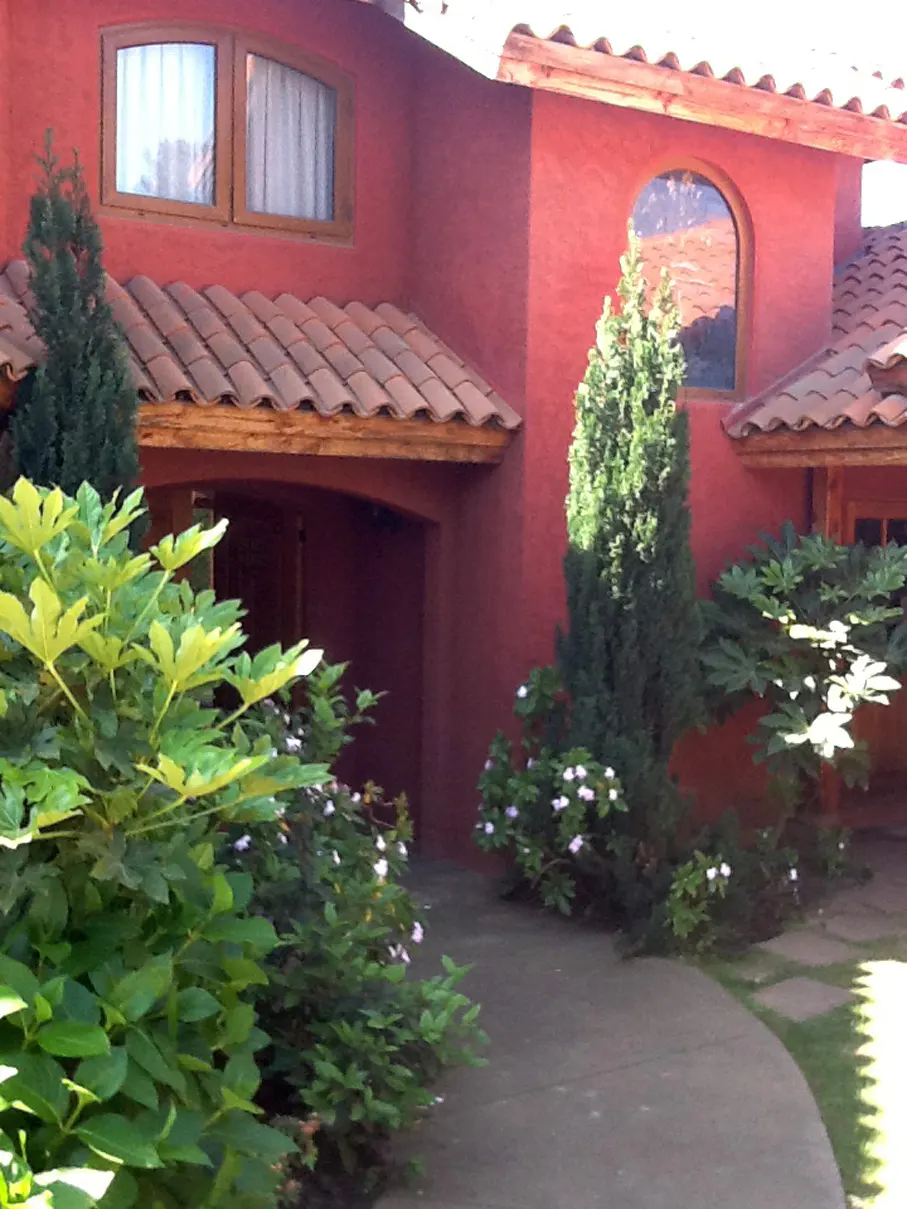 Exterior of a red stucco house with a brown tile roof, green bushes, and a curved walkway.