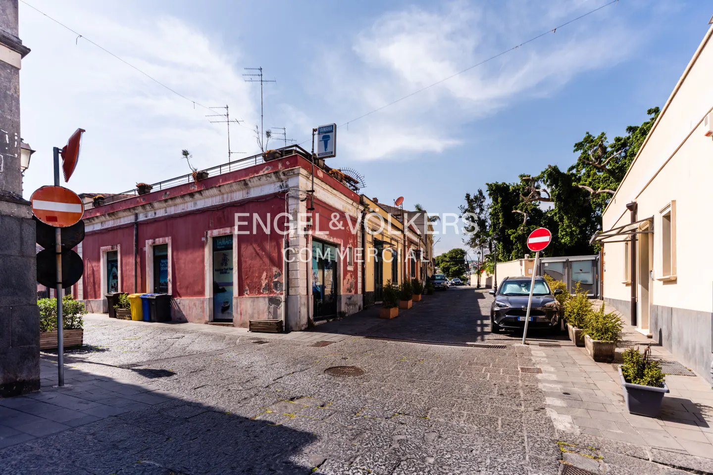 Street view of Engel & Volkers Commercial building in Catania, Italy. Red and yellow buildings line a cobblestone street.