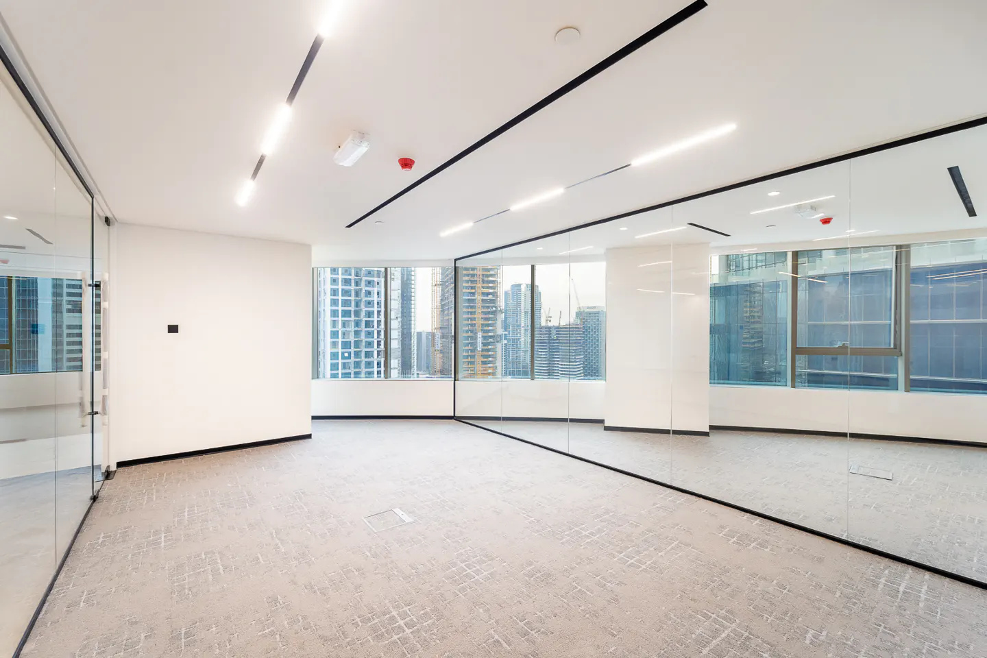 Empty office space with gray carpet, white walls, and floor-to-ceiling windows showing a city skyline.