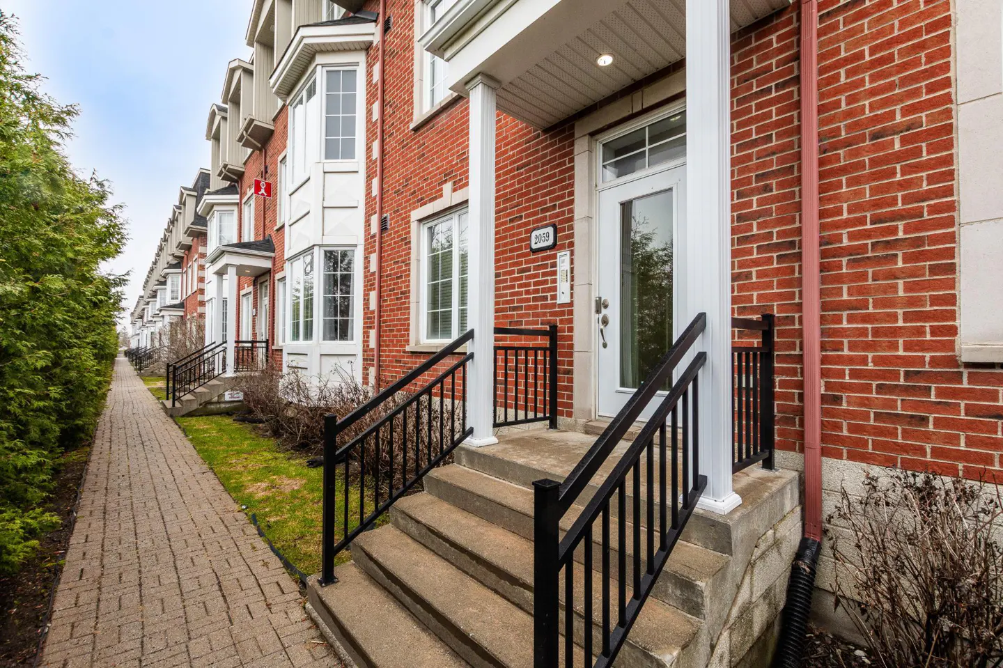Row of red brick townhouses with white trim. Concrete steps lead to a white front door with black railings.