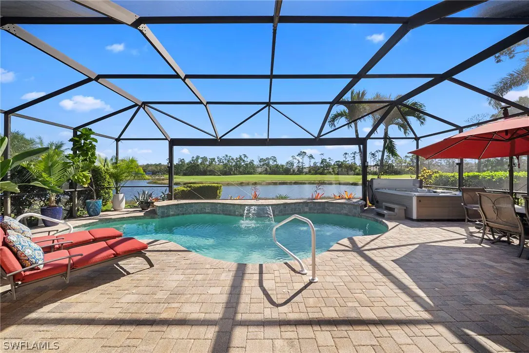 Screened-in pool area with red lounge chairs, a hot tub, and a red umbrella. A lake is visible in the background.