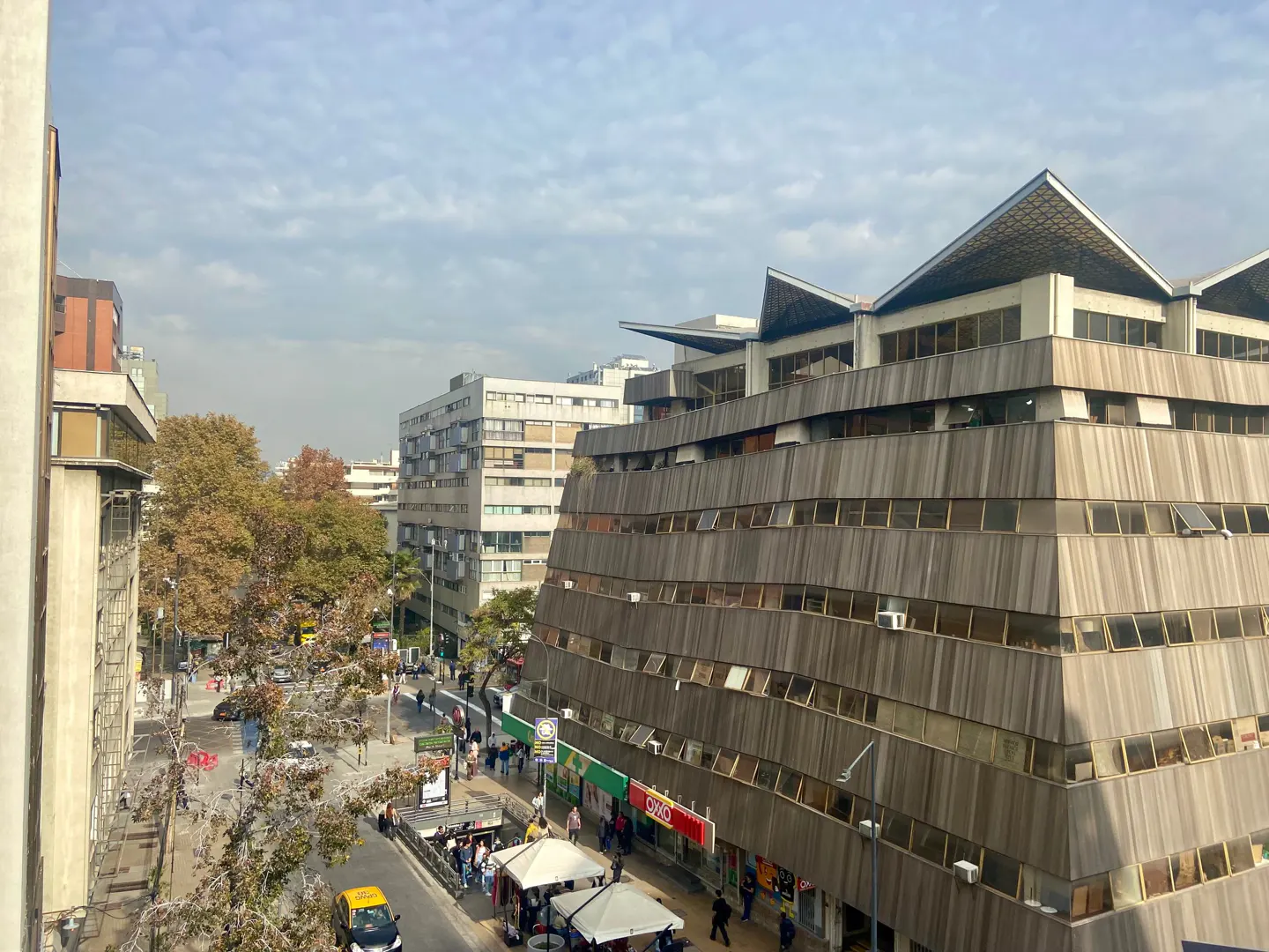 Cityscape view of a multi-story building with a unique stepped facade, street with pedestrians, and cloudy sky.