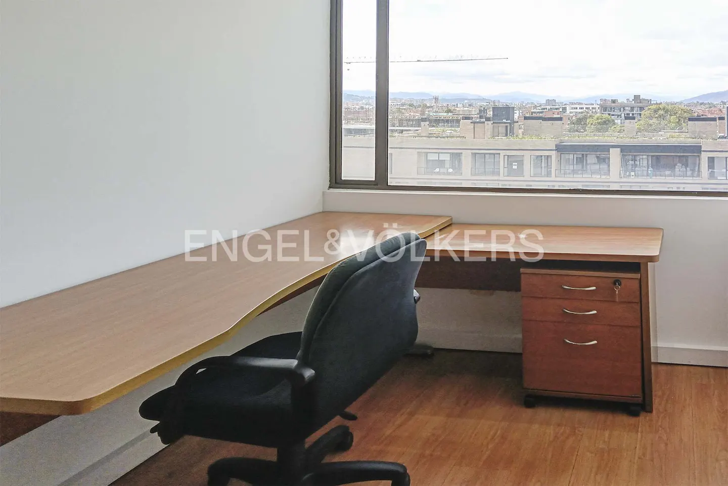 Office space with a wooden desk, black chair, and a window view of a cityscape.