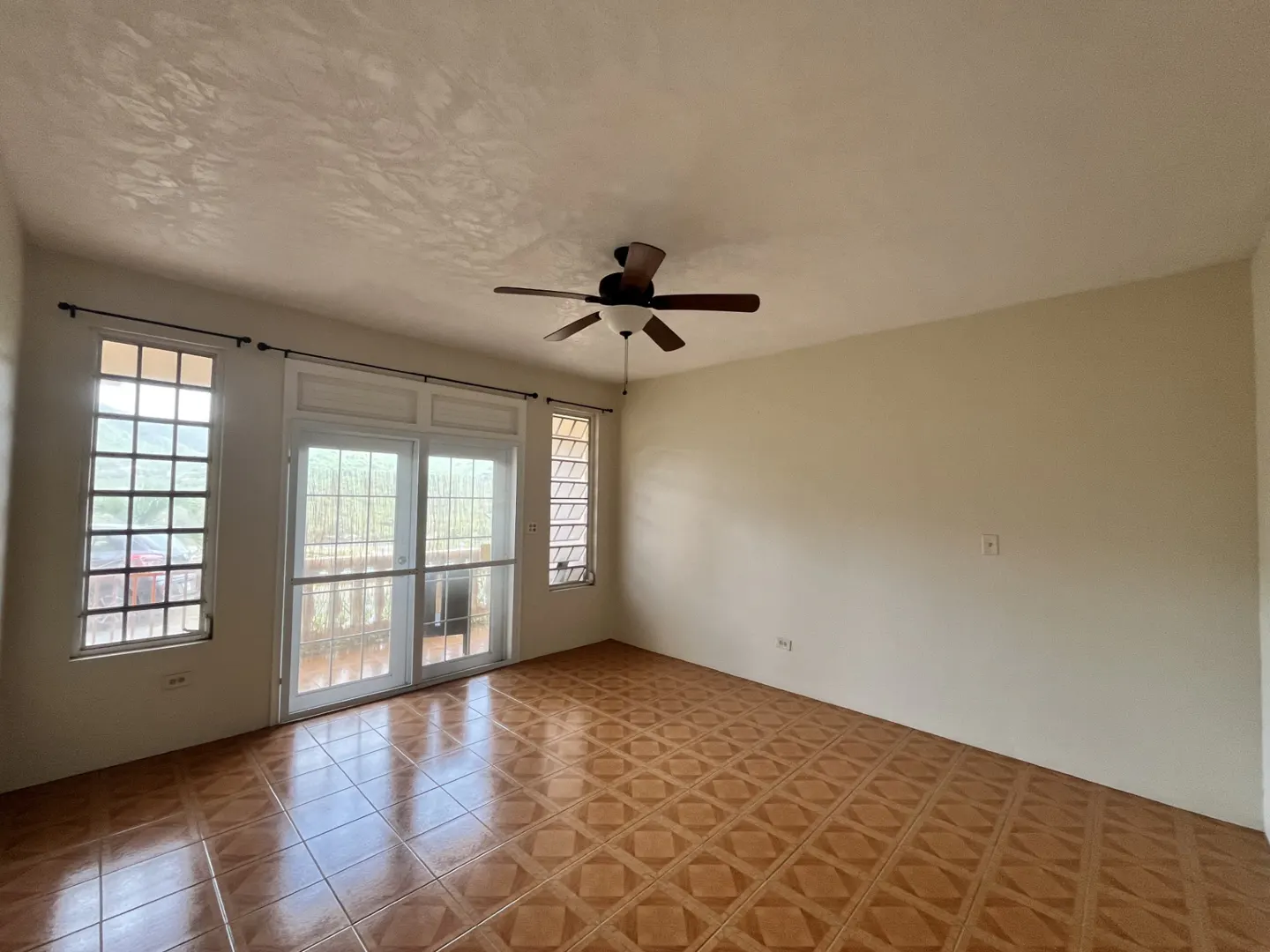 Empty room with beige walls, brown patterned tile floors, a ceiling fan, and glass doors leading to a balcony.