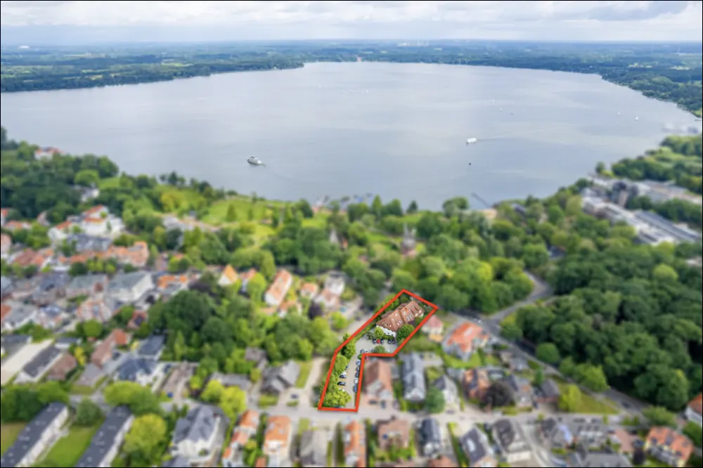 Aerial view of a property outlined in red, near a lake and trees.