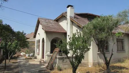 A single-family, one-story house with a brown tile roof, white walls, and a chimney. Trees are in the yard.
